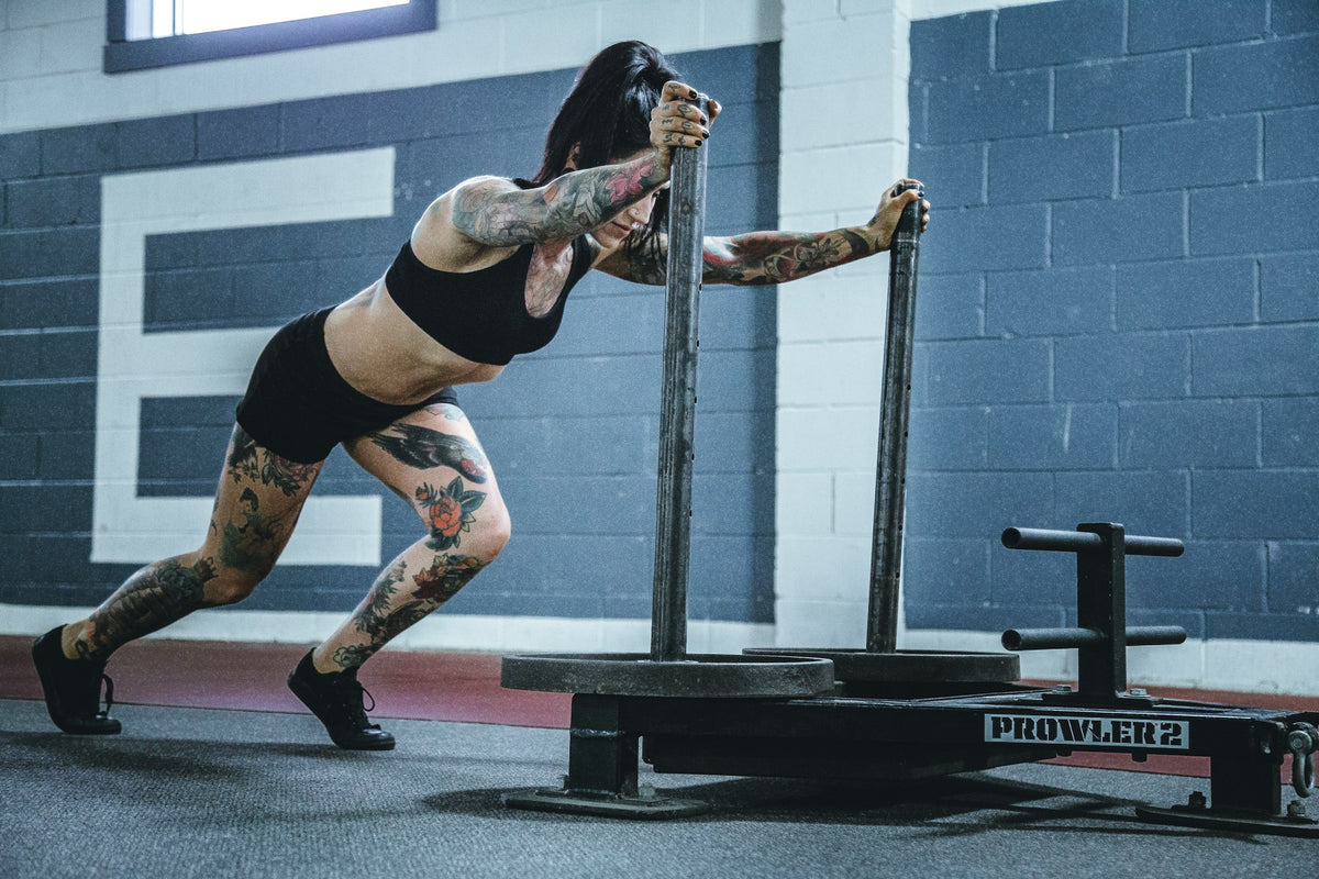 Kvinna pushar en viktad släde i ett gym
