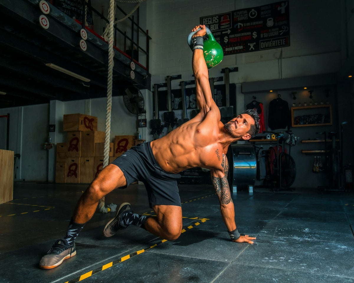 Man gör en kettlebell get-up i hårt solljus i ett gym