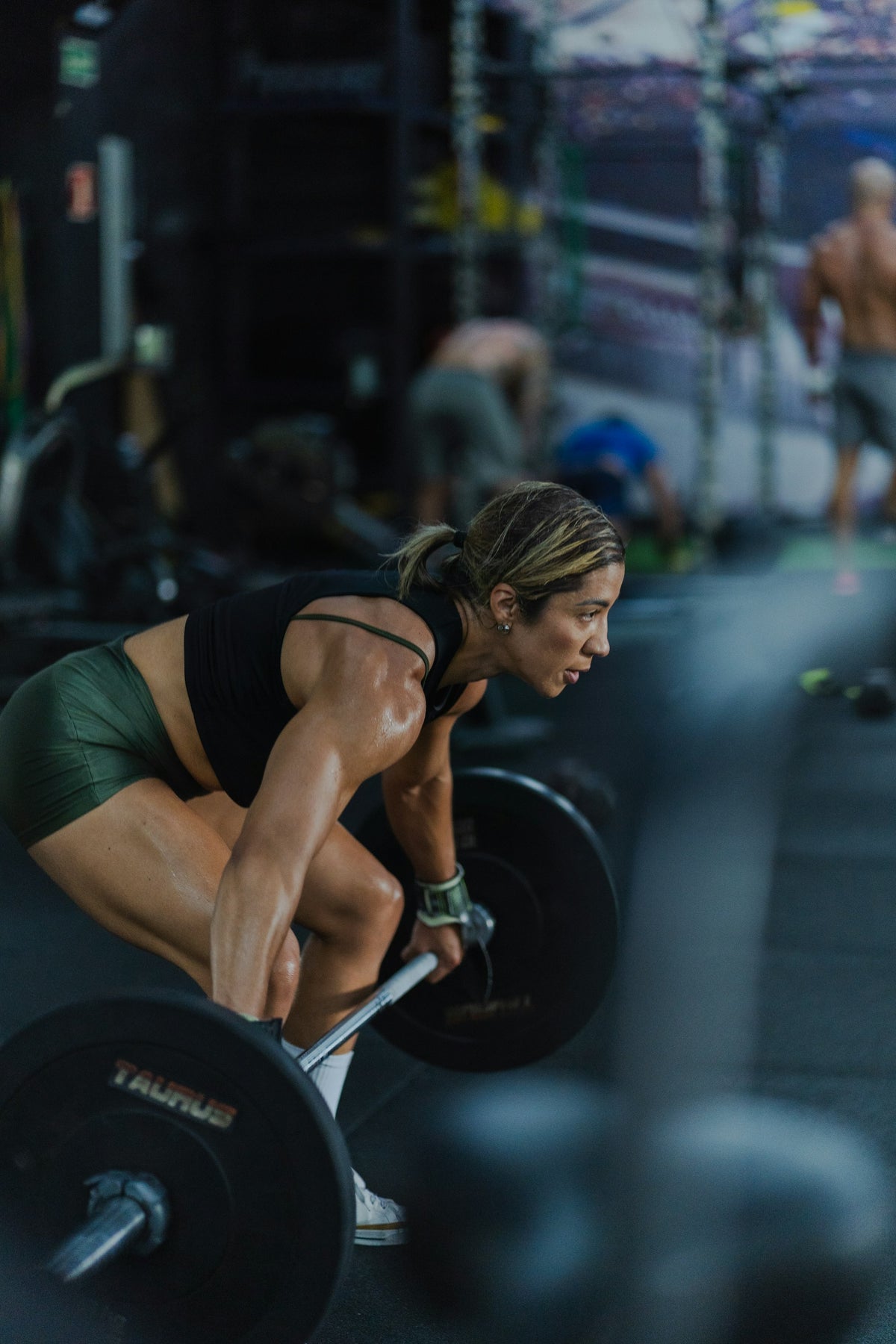Kvinna lyfter en tung skivstång i ett mörkt gym